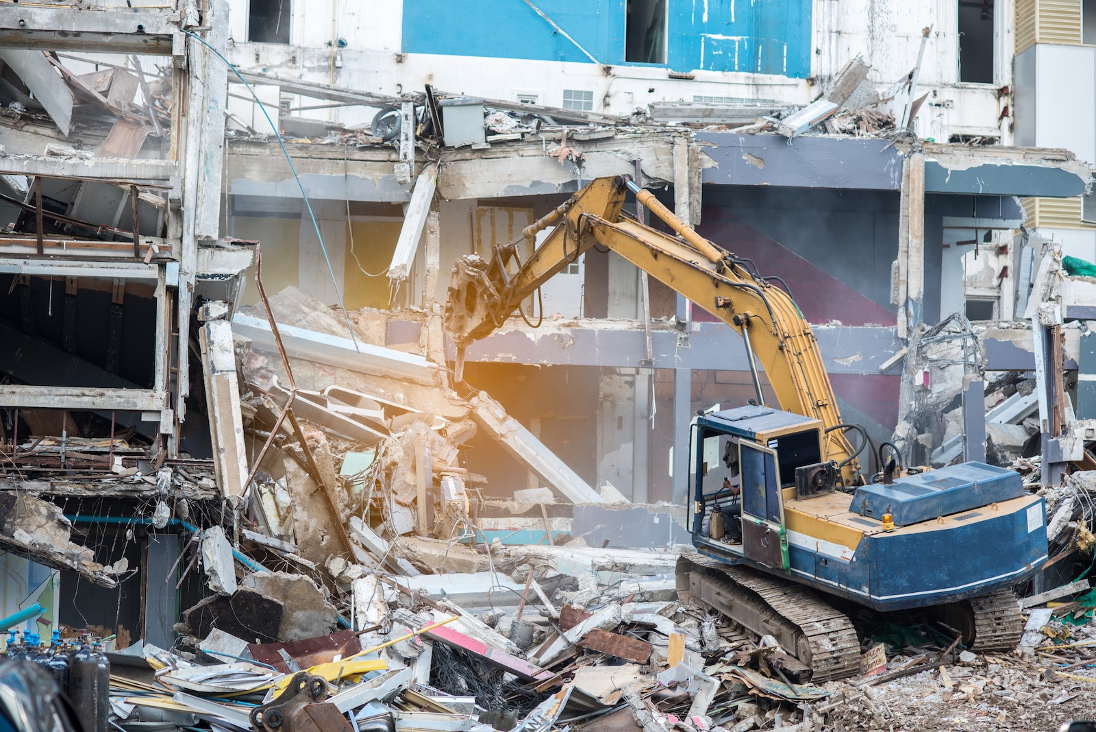 Worker controlling backhoe demolishing old buildings. Demolition site with pile of rubble and bulldozer at Bangkok site.