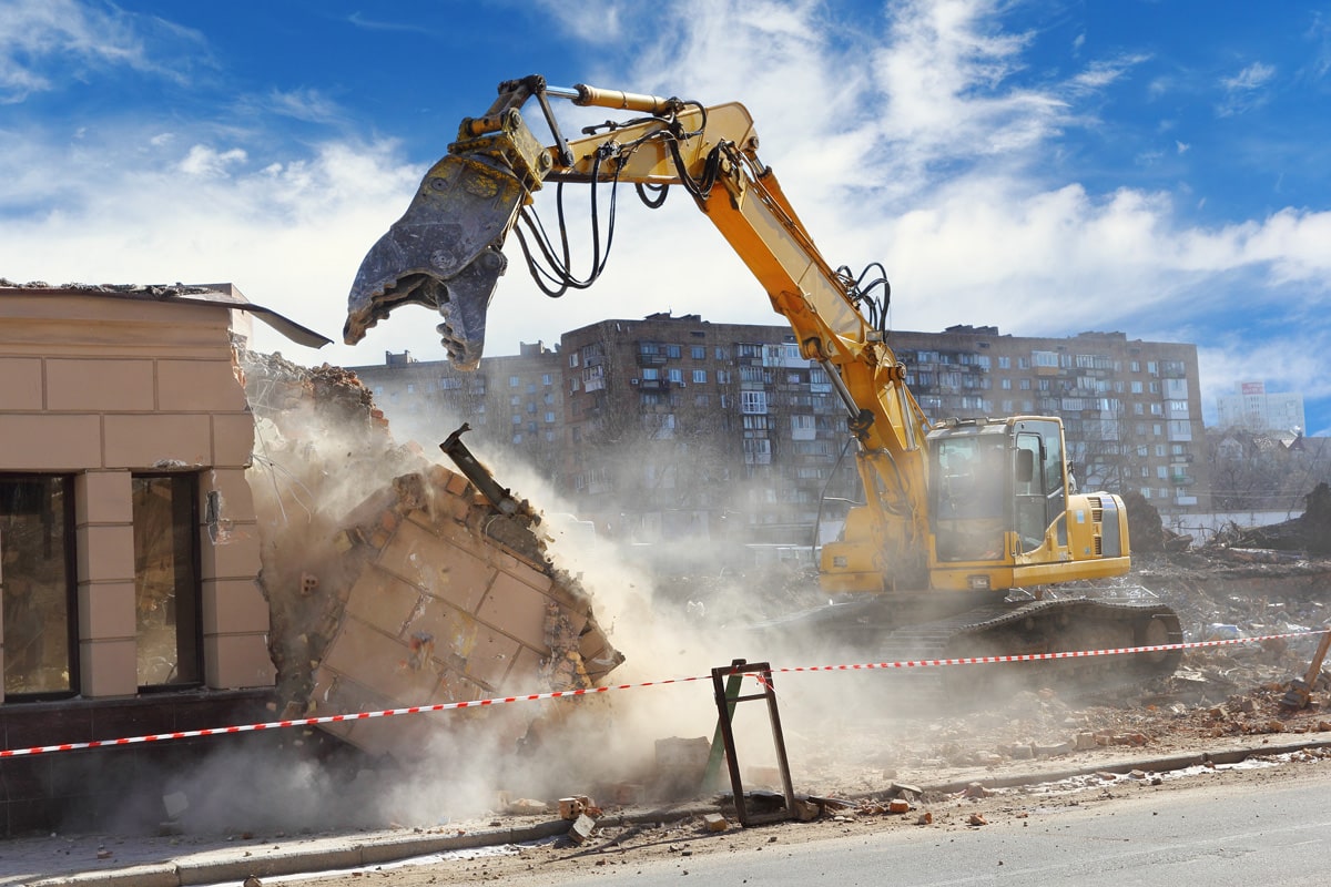 A yellow excavator tearing down a small building in El Paso.